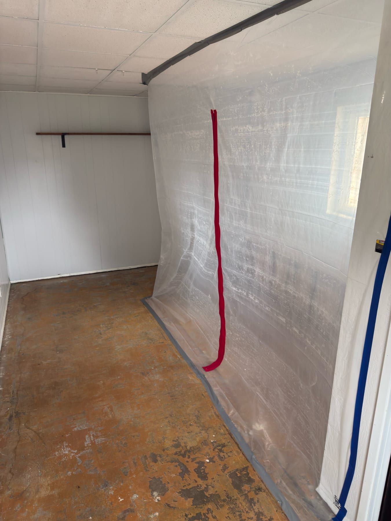 Clear plastic containment sheeting taped floor to ceiling across a room opening, with a zippered access seam.