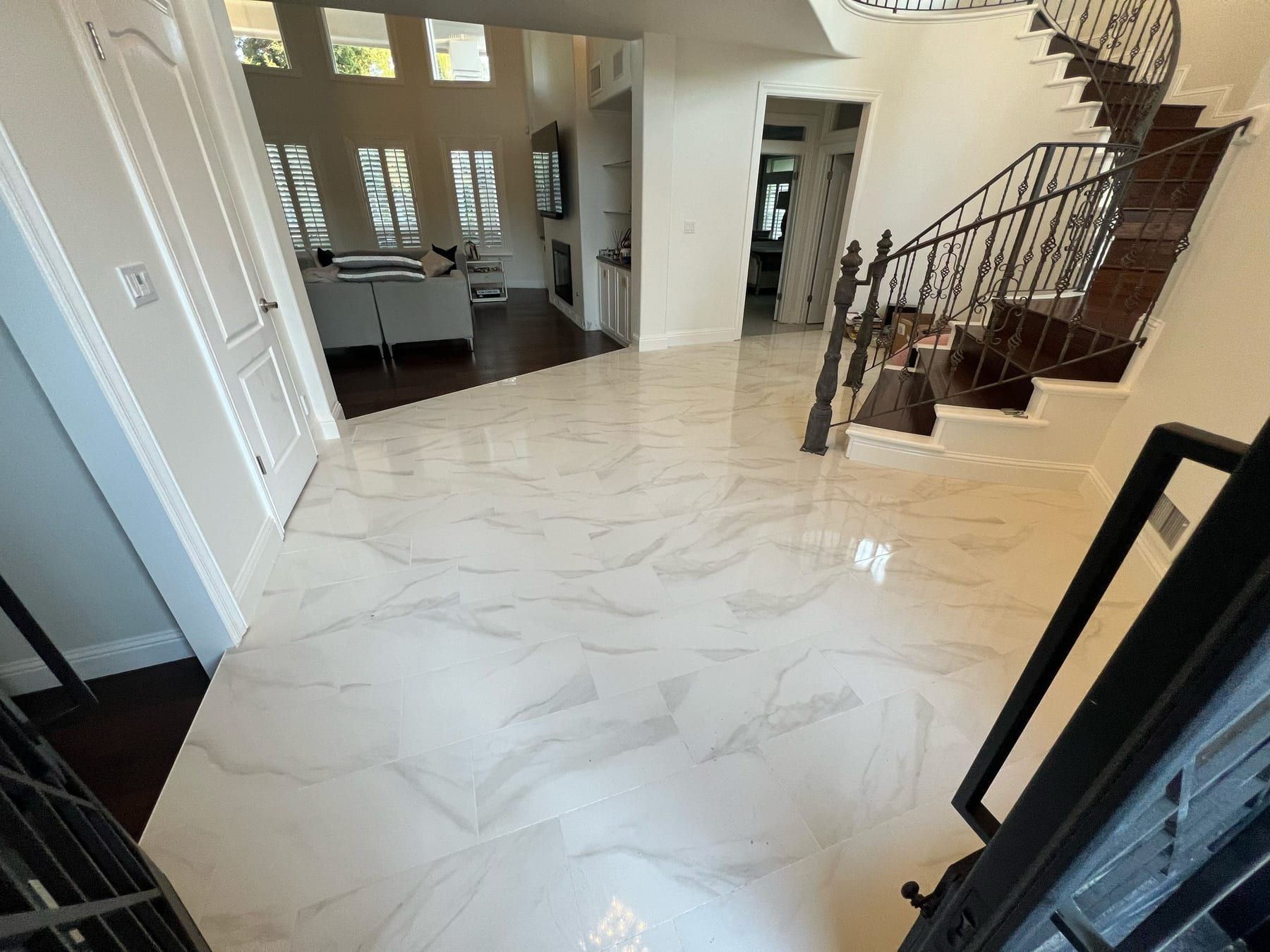 A home entryway with large-format marble-look tile flooring, a wrought-iron staircase railing, and an open living room beyond.
