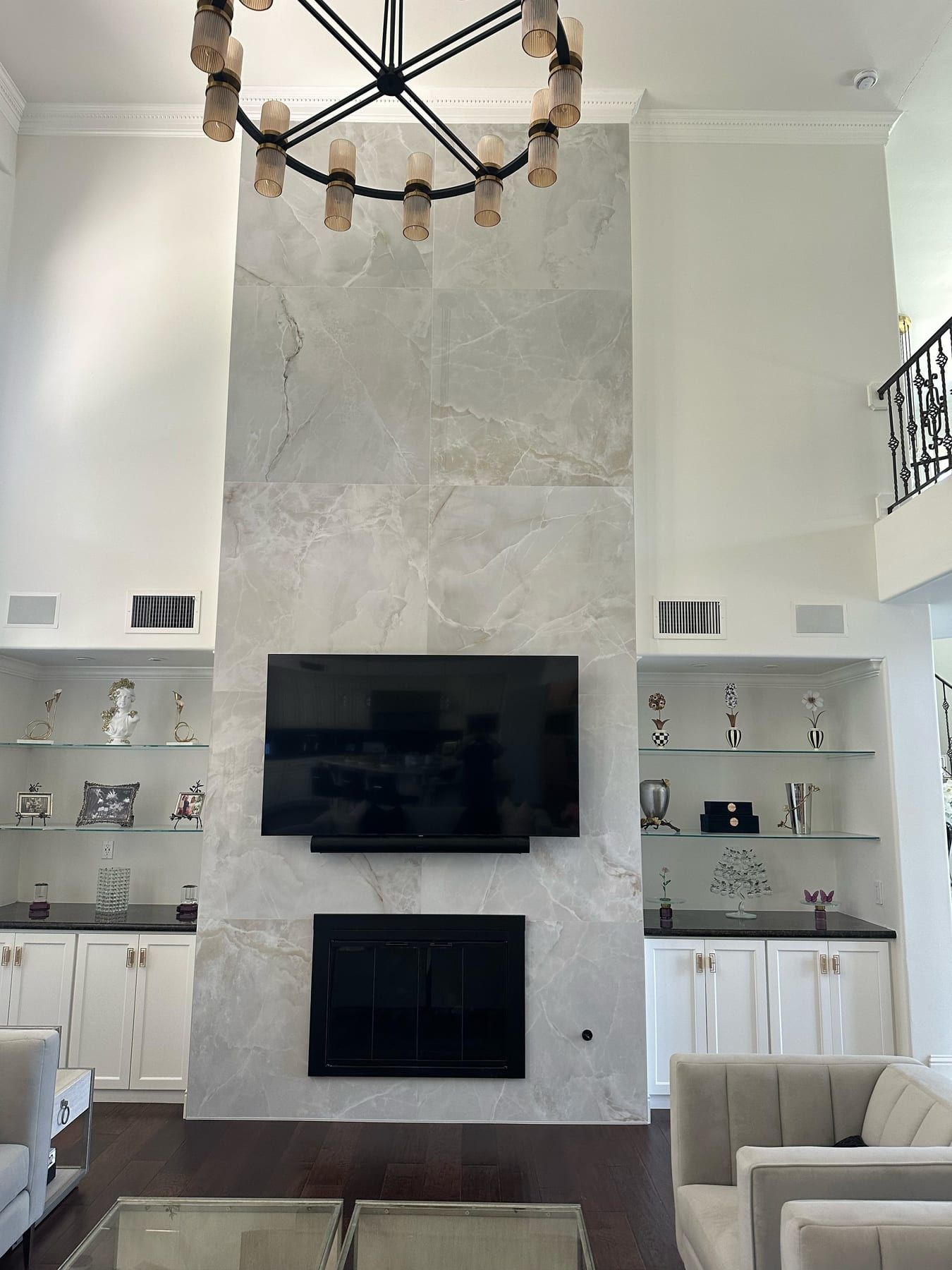 A tall marble-tiled fireplace wall with a mounted television and a black fireplace insert, flanked by built-in display shelves.